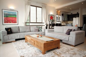 A modern living room with two sofas, a wooden coffee table, and a kitchen in the background. - Panoramic Ocean View 1 min From the Sea (Tel Aviv)
