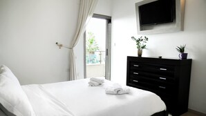 A neatly made bed with white linens and two towels, a black dresser with a flat-screen TV above it, and a potted plant on the dresser. - Panoramic Ocean View 1 min From the Sea (Tel Aviv)