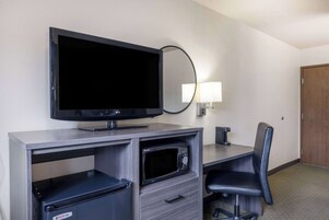 Habitación de hotel con televisión de pantalla plana, microondas, escritorio con silla y lámpara.
