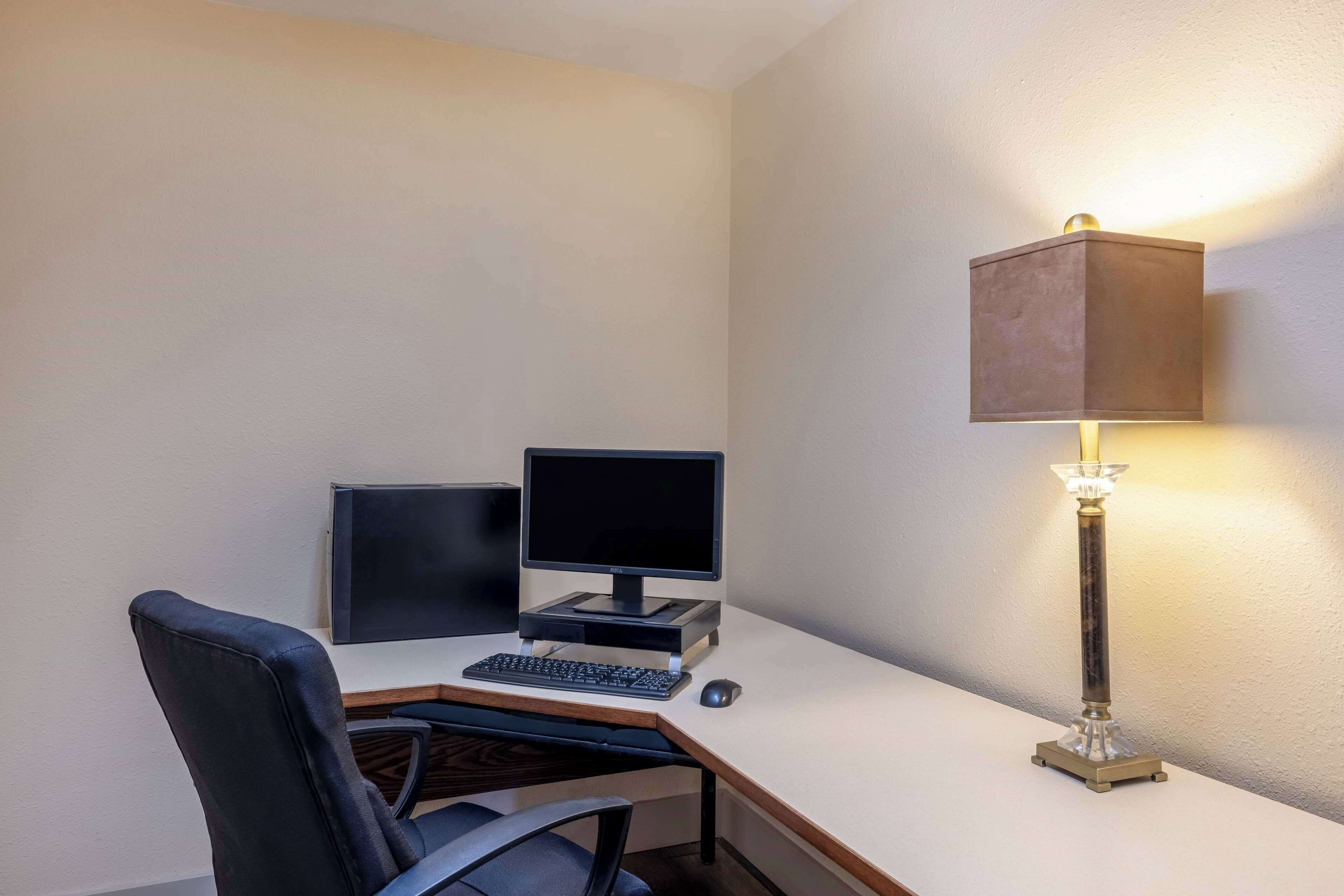 Un espacio de trabajo pequeño y ordenado, con un escritorio, dos monitores, un teclado, un ratón y una lámpara de escritorio.