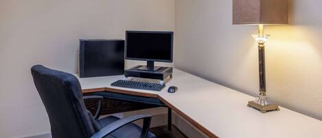 Un espacio de trabajo pequeño y ordenado, con un escritorio, dos monitores, un teclado, un ratón y una lámpara de escritorio.