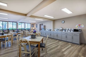 Un comedor amplio con mesas y sillas de madera, una cocina con electrodomésticos modernos y ventanas grandes que ofrecen luz natural.