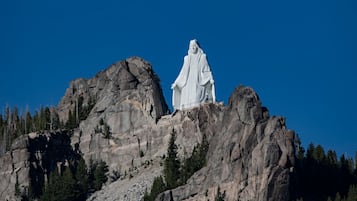 Eine große weiße Statue auf einem felsigen Berggipfel, umgeben von vereinzelten Bäumen.