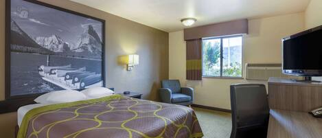 A hotel room with a large bed, a desk, a chair, a television, and a window with a view of mountains.