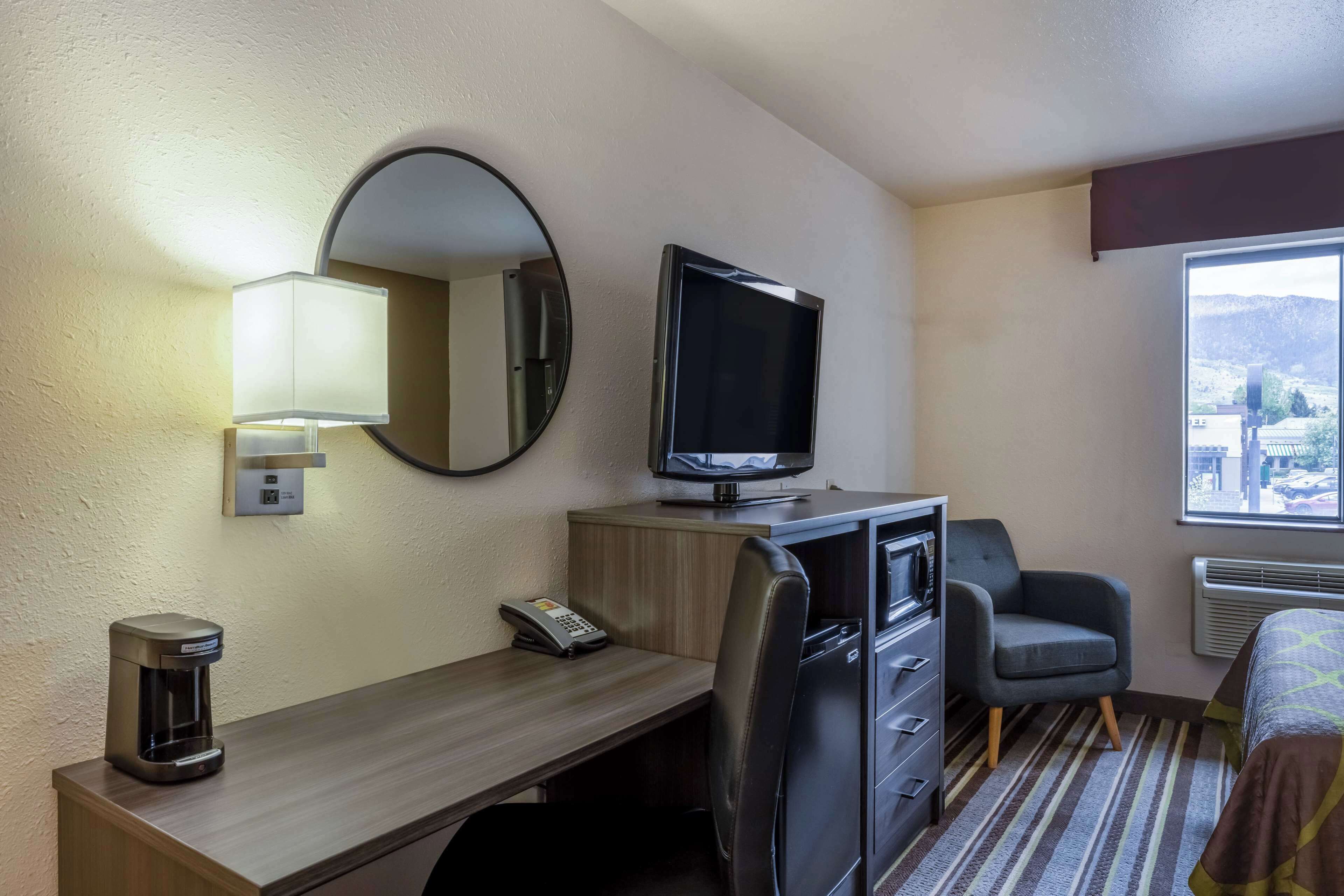 Une chambre d’hôtel équipée d’un bureau, d’une télévision, d’un miroir, d’une machine à café, d’une chaise, d’un lit et d’une fenêtre donnant sur un paysage agréable.