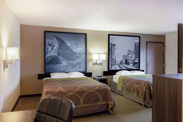 A hotel room with two beds, a desk, a chair, and a nightstand with a lamp.