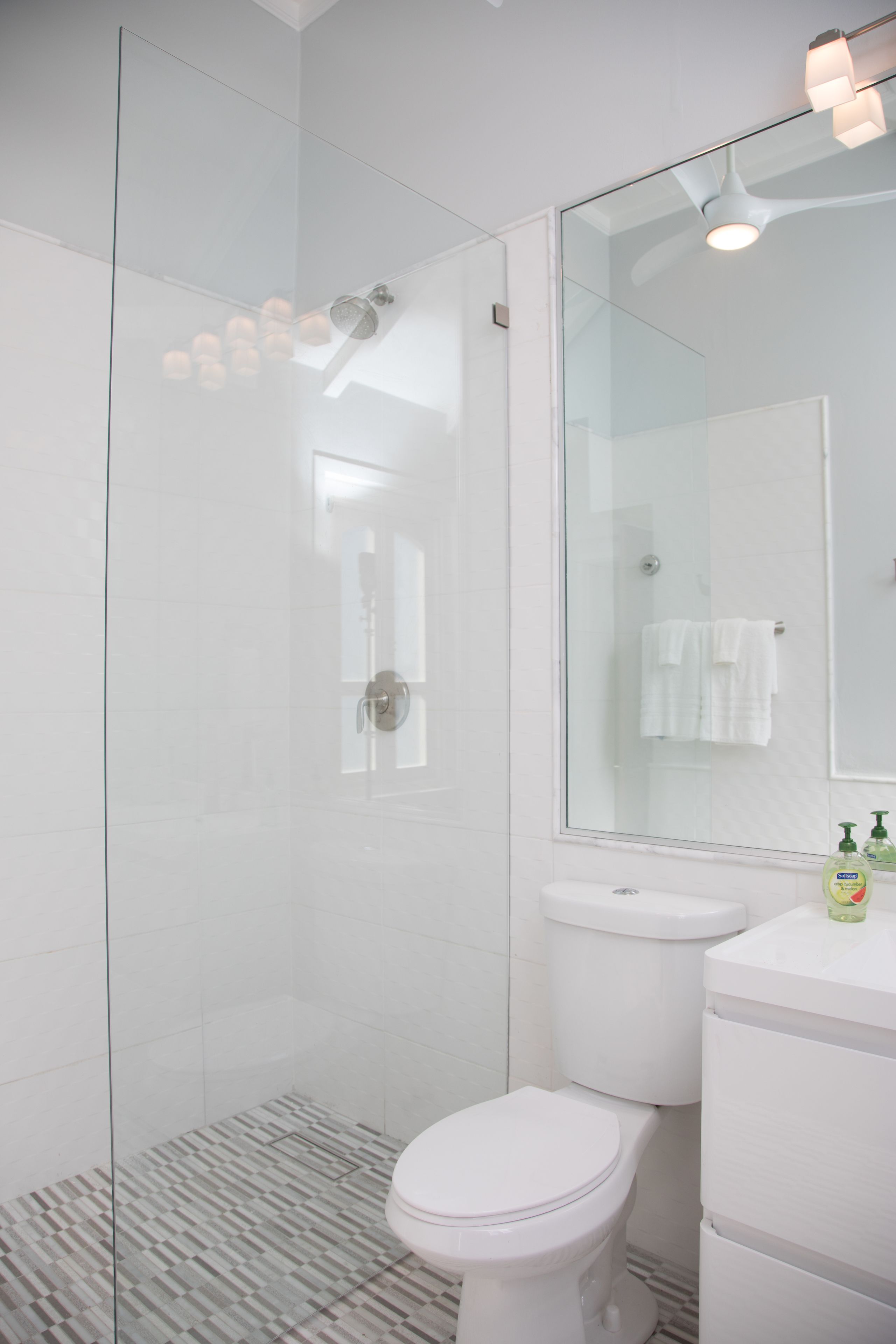 A modern bathroom with a glass shower enclosure, a white toilet, and a vanity with a mirror.