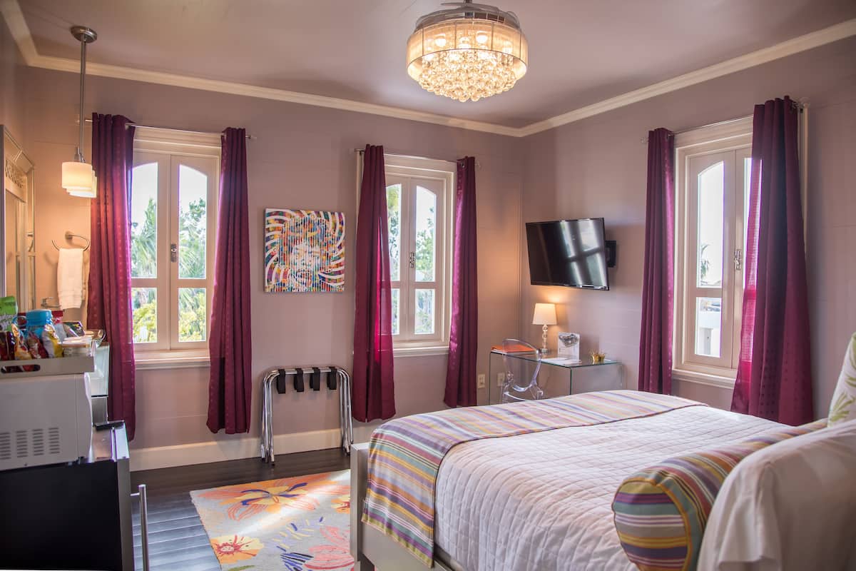 A bedroom with a bed, a TV, a desk, and a window with curtains.