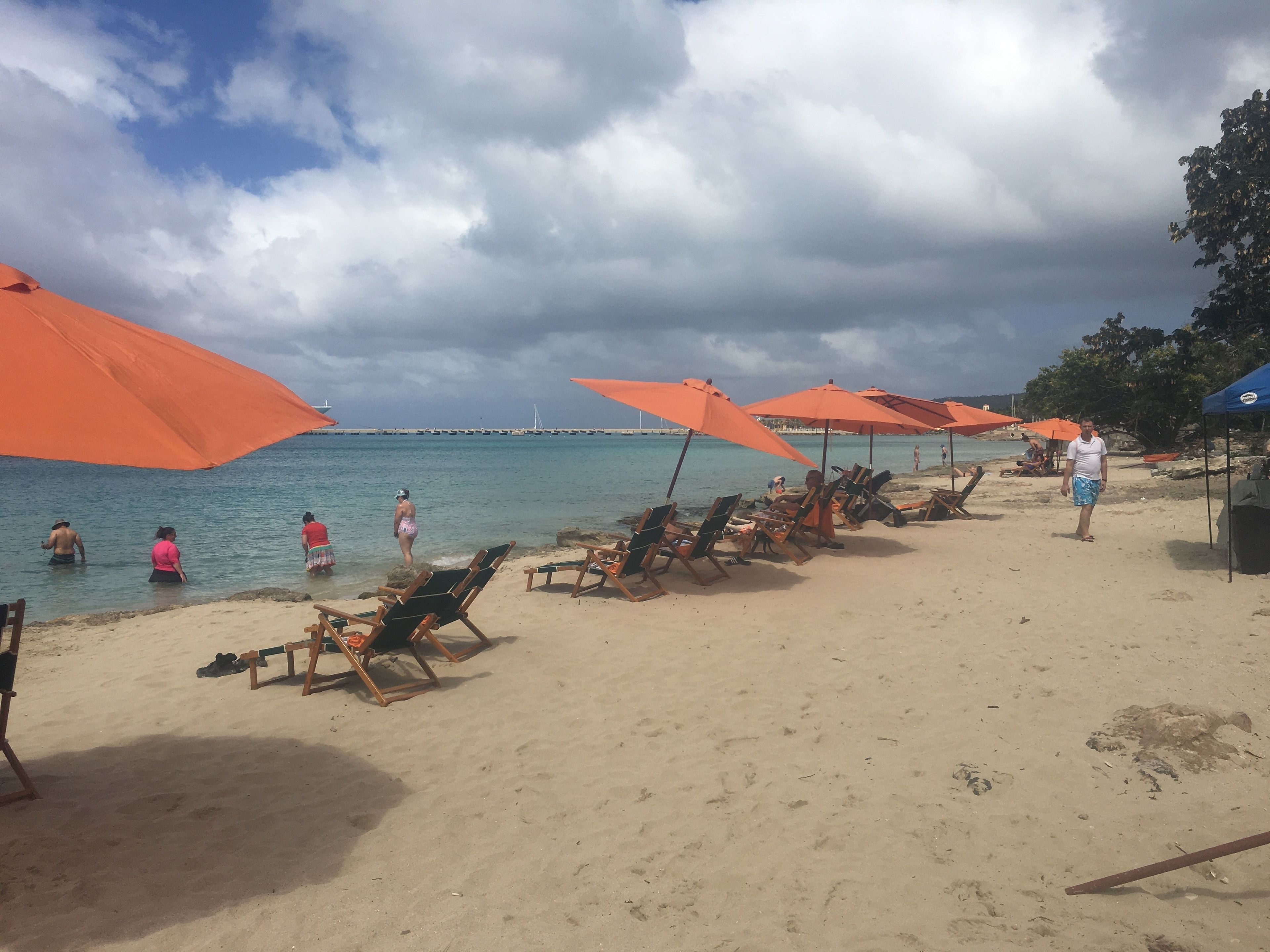 Una spiaggia con file di lettini e ombrelloni arancioni, un litorale sabbioso e il mare sullo sfondo.