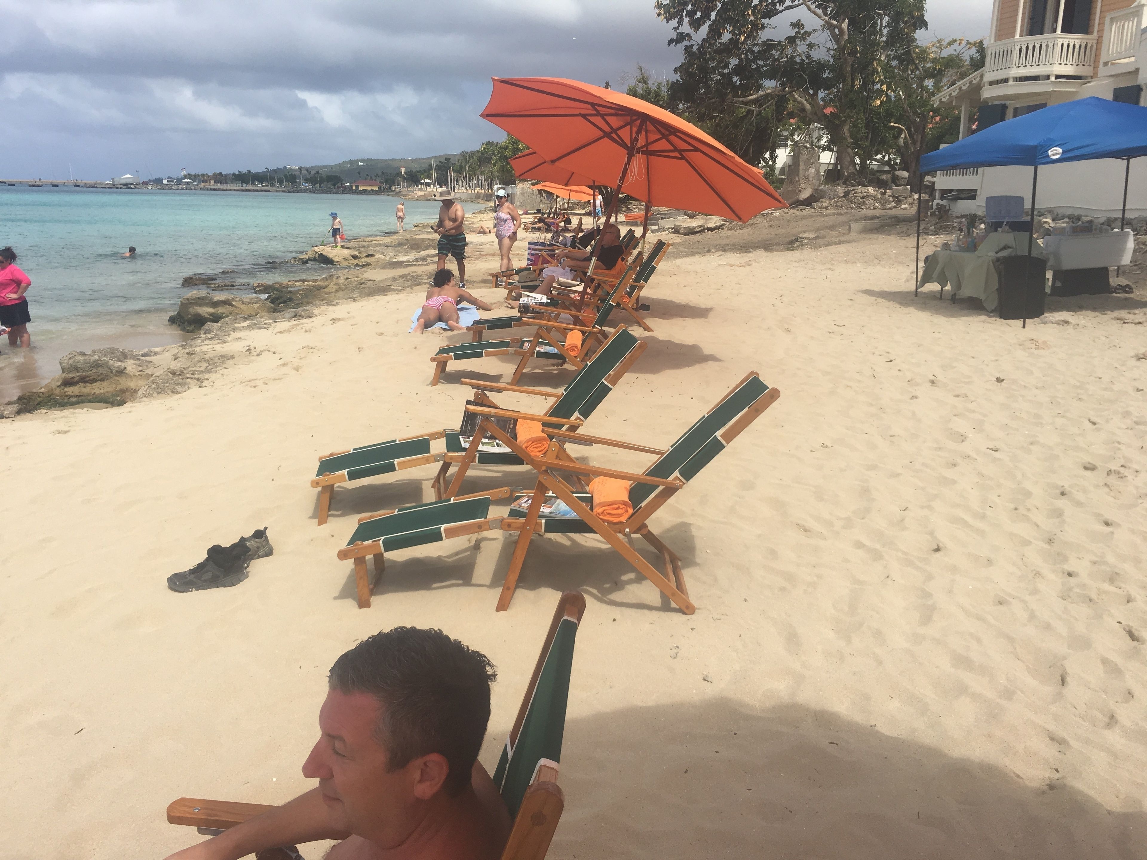 Ein Strand mit Reihen aus Holzliegen und einem orangefarbenen Sonnenschirm.