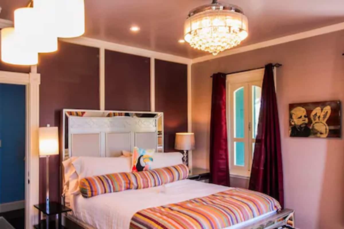A bedroom with a large bed, a chandelier, and a window with curtains.