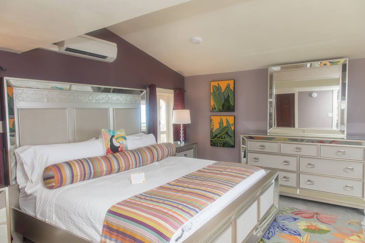 A bedroom with a bed, nightstands, a dresser, a mirror, and wall art.