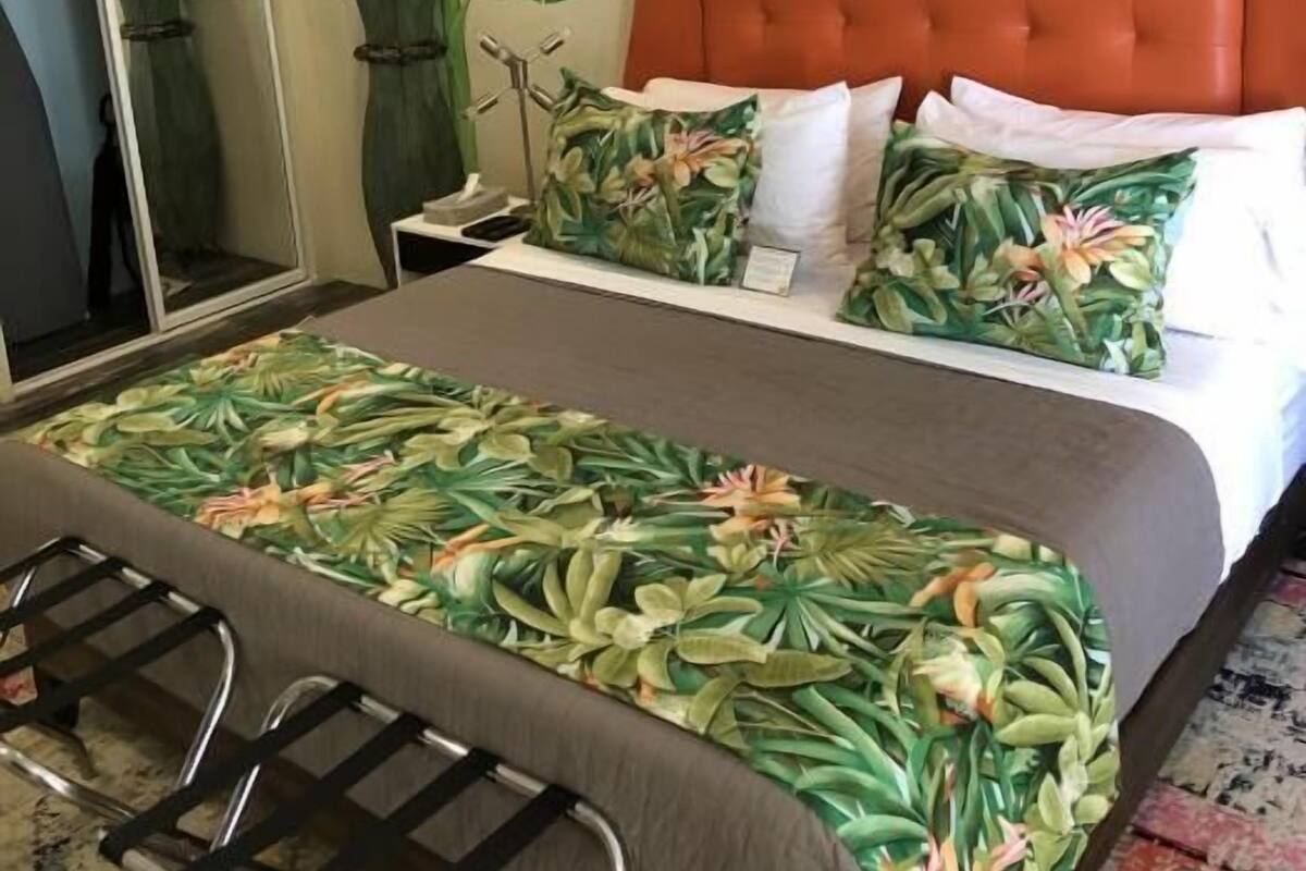 A hotel room with a large bed, an orange headboard, a mirror, and a large plant.