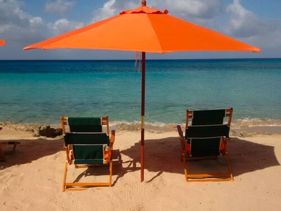 Two beach chairs under an orange umbrella on a sandy beach with a clear blue ocean in the background.