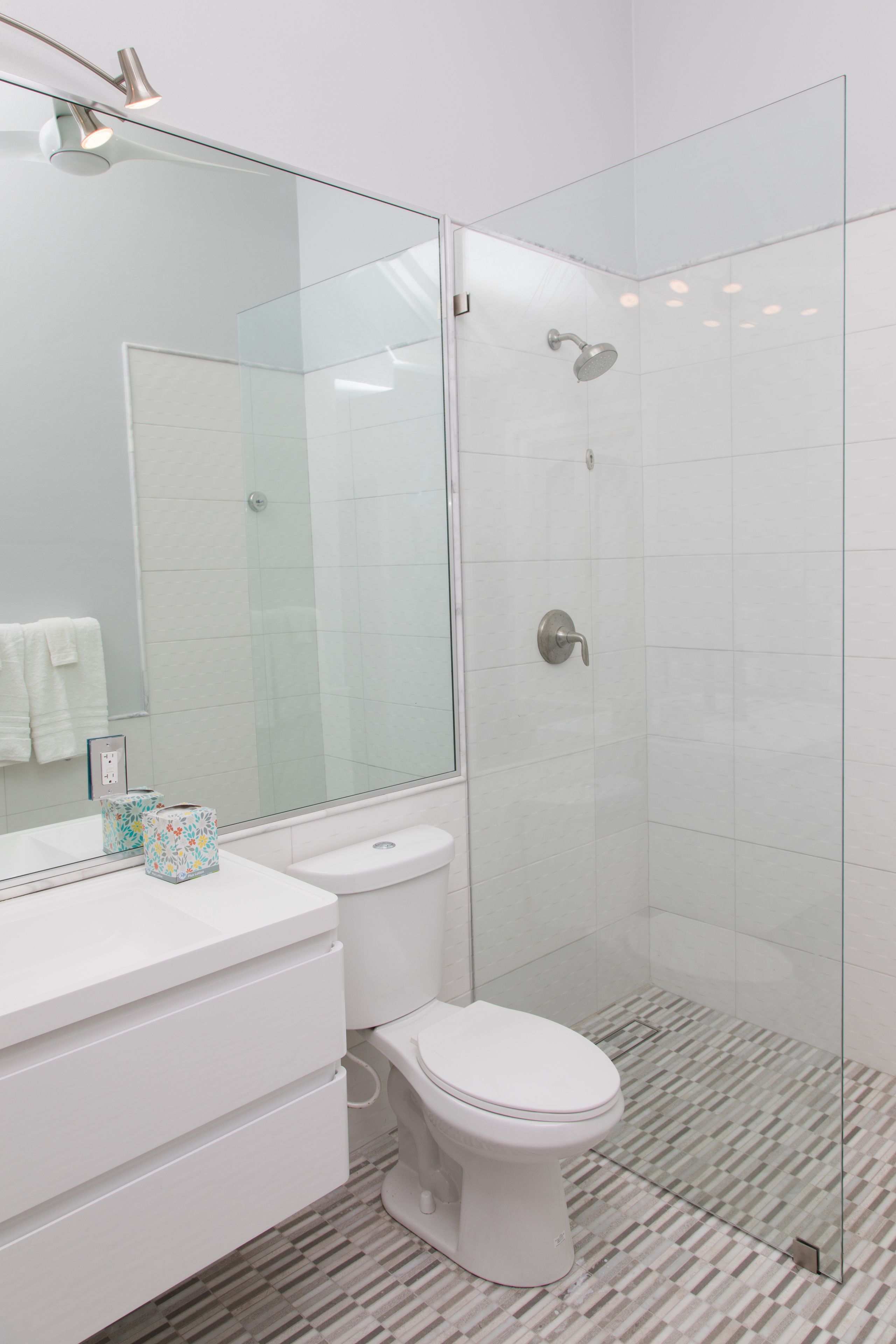 A modern bathroom with a glass-enclosed shower, a white toilet, and a vanity with a mirror.