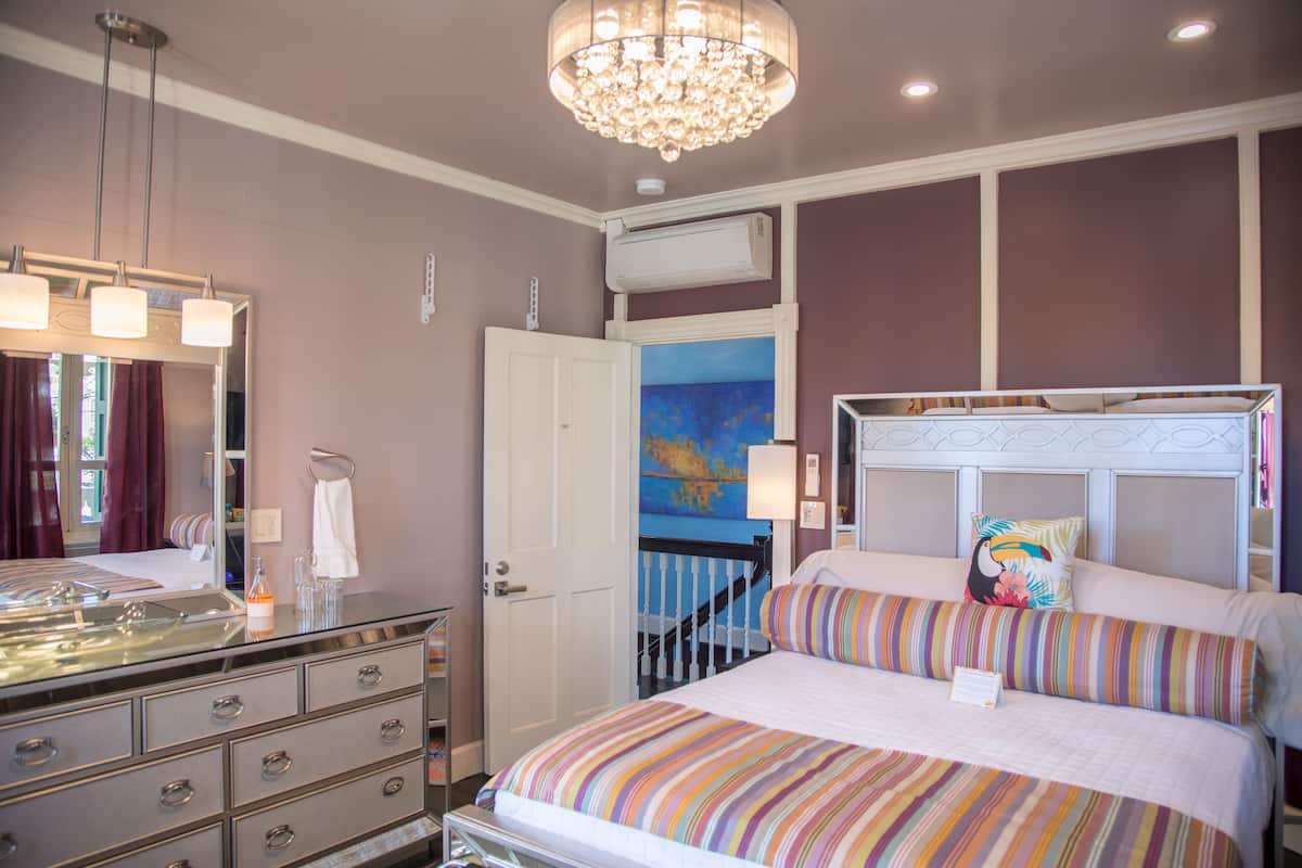 A bedroom with a large bed, a dresser, a mirror, a chandelier, and a painting on the wall.