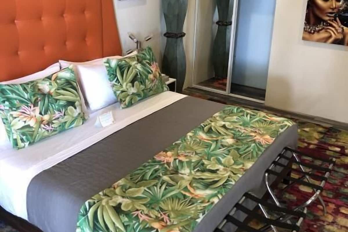 A hotel room with a tufted orange headboard, a bed with floral-patterned bedding, a shower area, and a patterned carpet.