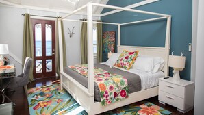 A four-poster bed with a floral bedspread, a bedside table with a lamp, and a view of the sea through a door. - The Fred - Adults Only (Frederiksted)