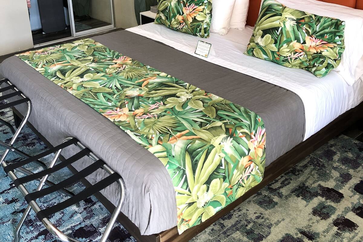 A hotel room with a large bed, an orange headboard, a mirror, a nightstand, and a shower area.