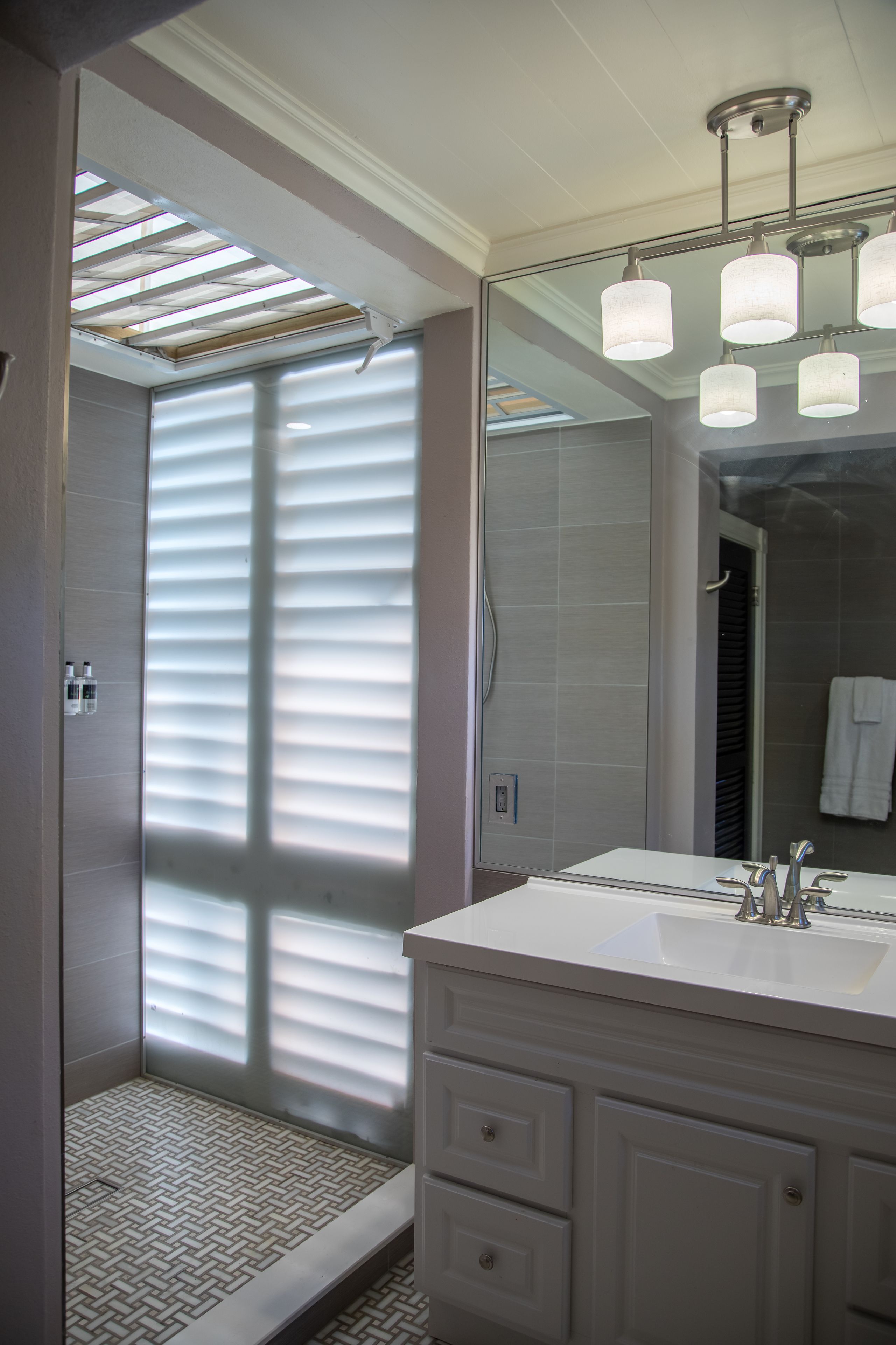A modern bathroom with a walk-in shower, a large mirror, and a white vanity.