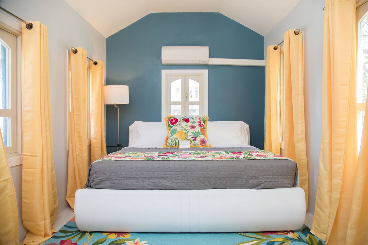 A bedroom with a bed, curtains, a window, and an air conditioning unit.