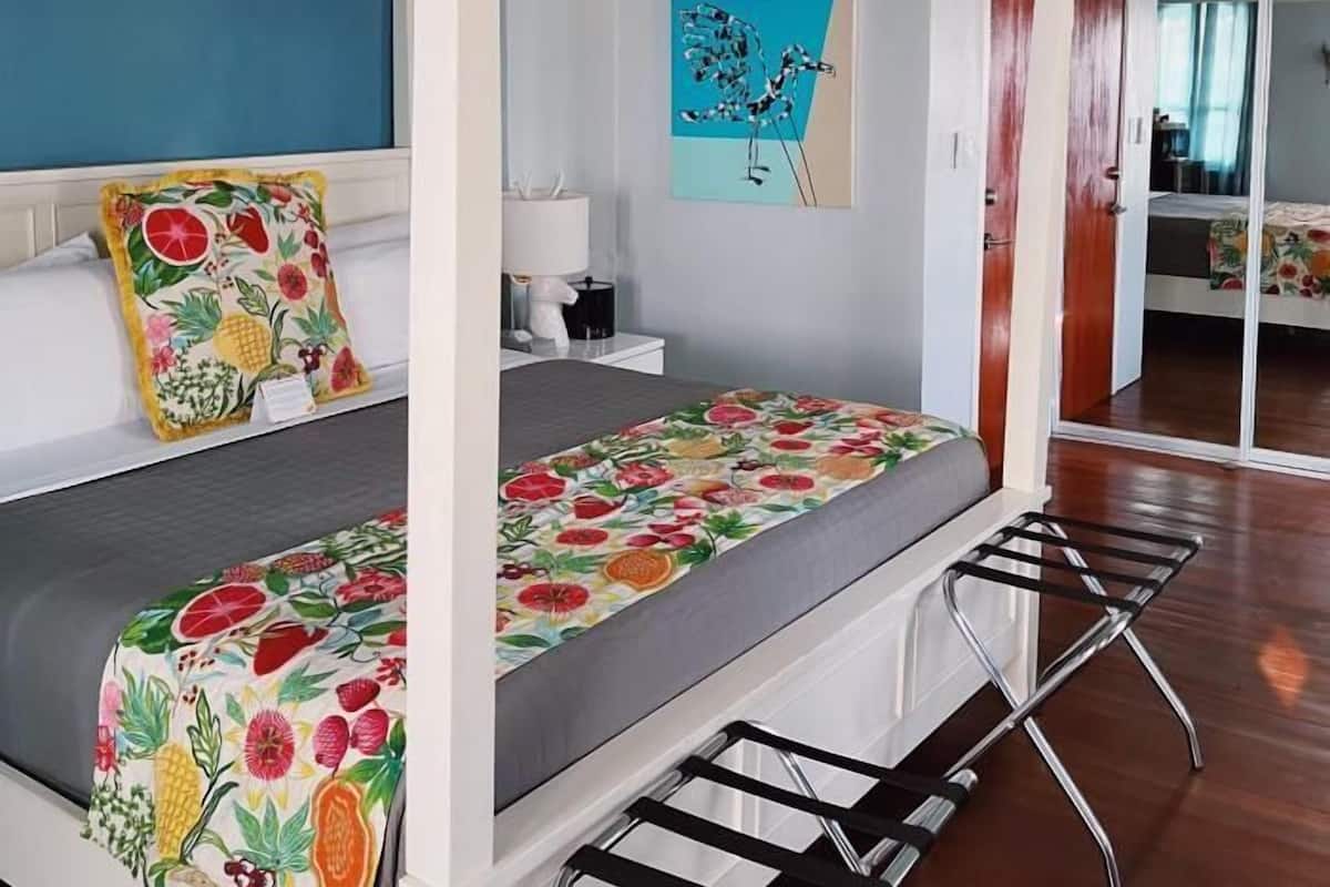 A bedroom with a four-poster bed, a nightstand, a lamp, a painting, and a sliding door leading to another room.