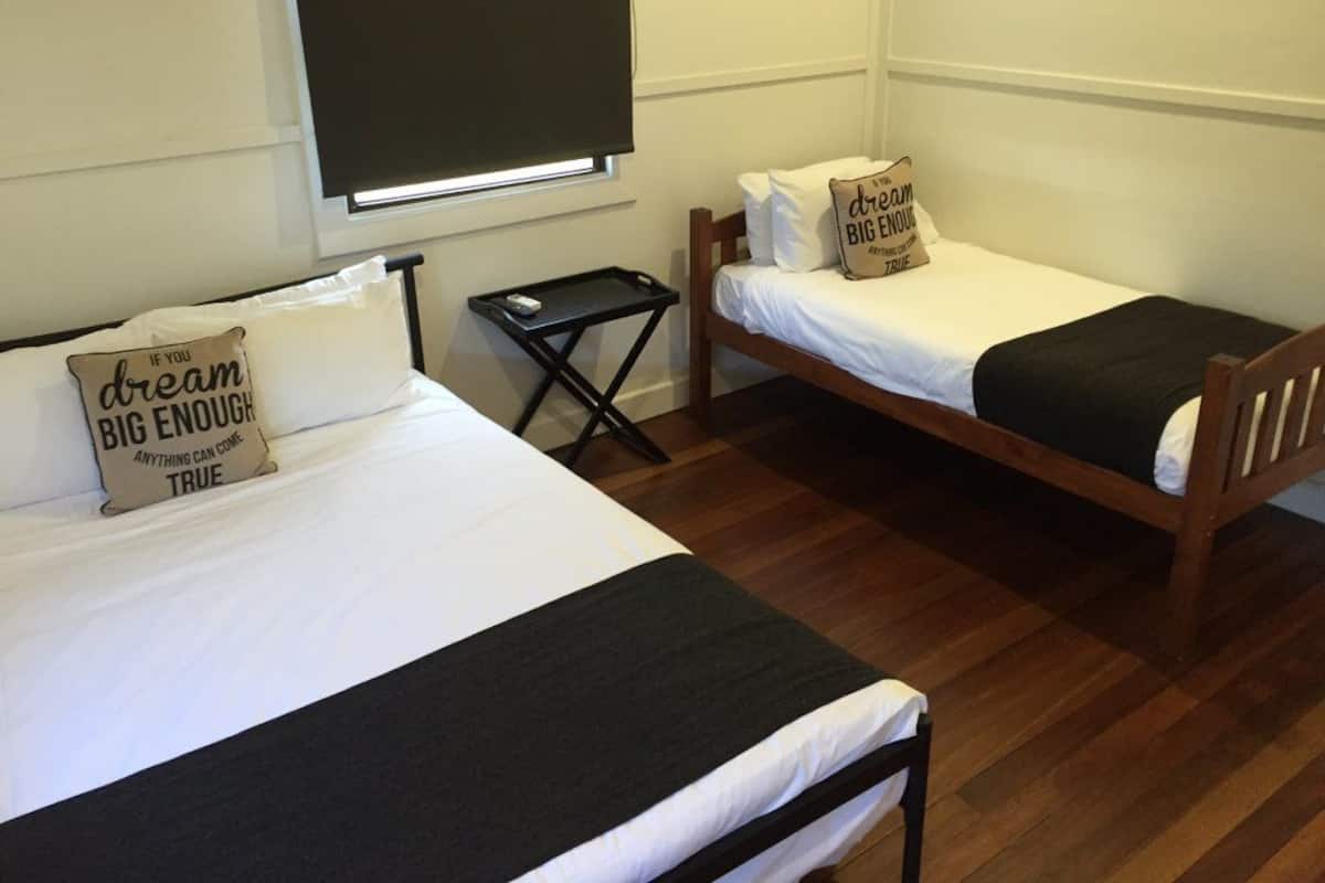 Habitación con dos camas individuales, cada una con un almohadón con citas motivacionales. Hay una mesita entre las camas y una ventana con una persiana bajada a medias.
