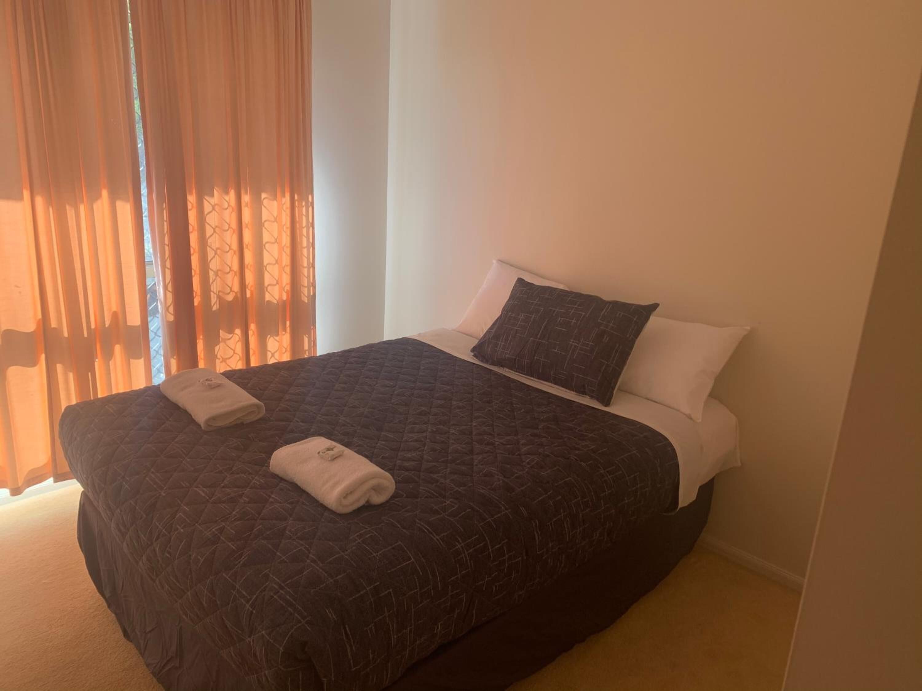 Una cama bien hecha con un edredón acolchado oscuro, dos almohadas y una toalla doblada sobre la cama.