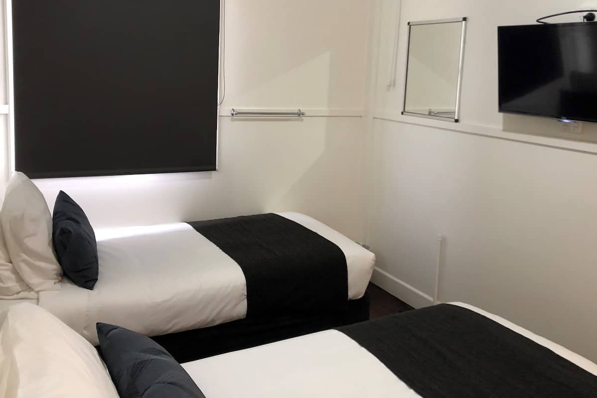 Una habitación de hotel con dos camas, televisión, ventana con cortina y puerta.