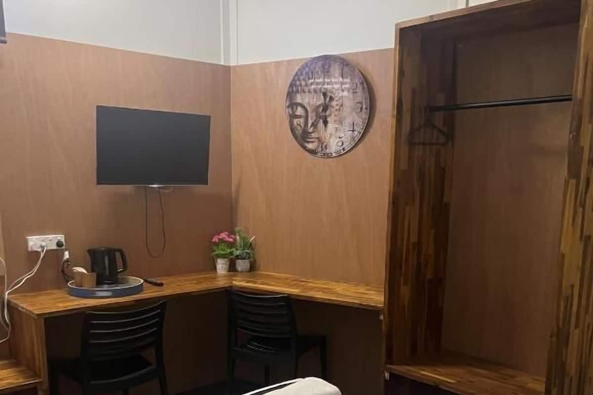 Habitación de hotel con cama, escritorio con silla, televisor montado en la pared y armario de madera.
