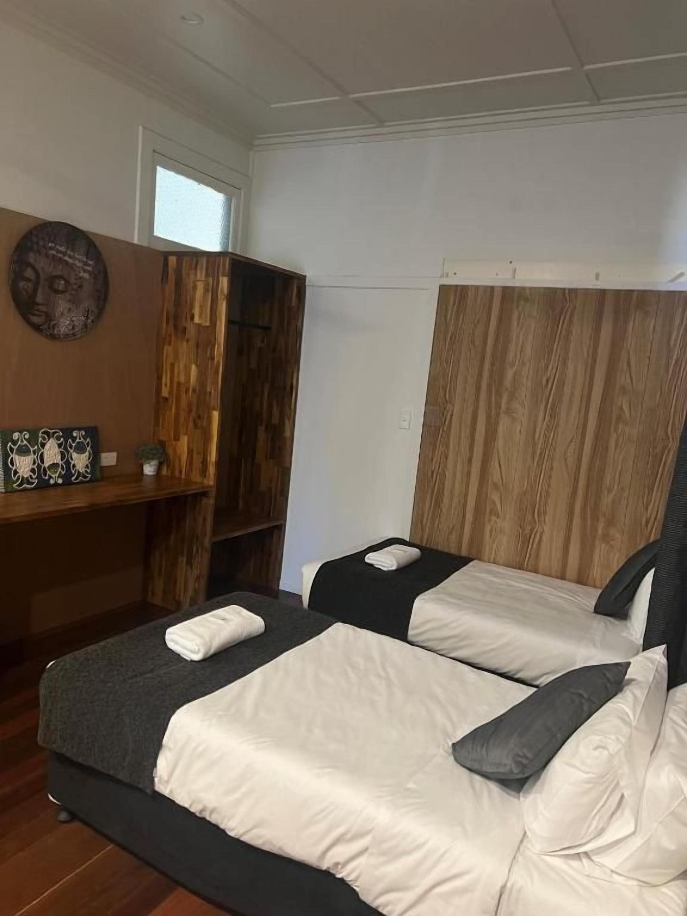 Una habitación con dos camas, un panel de madera en la pared, una estantería con adornos y una ventana.