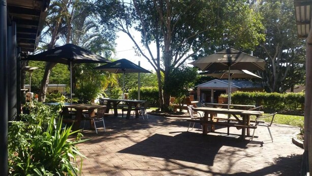 Un patio al aire libre con varias mesas de picnic y sombrillas, rodeado de abundante follaje y árboles.
