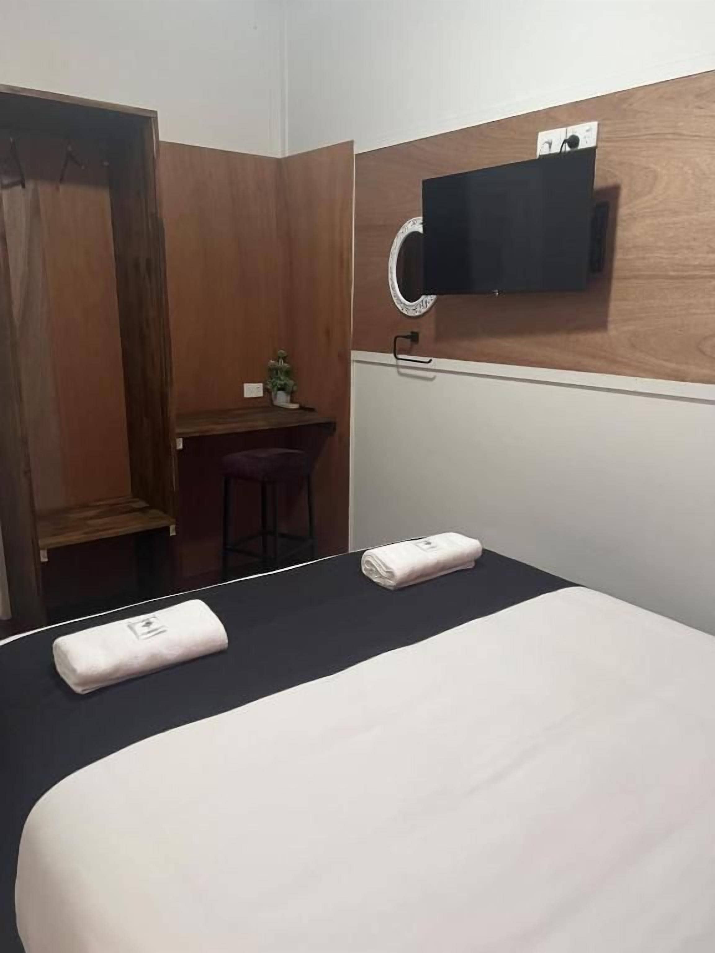A hotel room with a bed, a desk, and a small stool.
