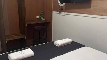 A hotel room with a bed, a desk, and a small stool.