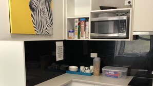 Una cocina compacta con armarios blancos, un microondas, una estufa y una encimera negra. Hay dos taburetes negros y una pared amarilla con estampado de cebra.