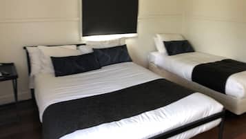 A room with two beds, each with white bedding and black headboards. There is a small table beside one bed and a wall-mounted shelf above the other bed.