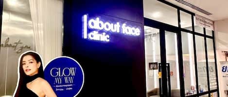 A storefront with a sign reading 'About Face Clinic' and a large poster for 'Glow My Way' by Juvejoy.