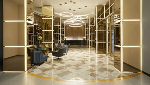 A modern lobby with a geometric patterned floor, a seating area with sofas and a coffee table, and a contemporary chandelier.