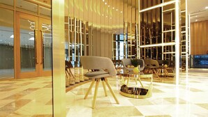 A modern lobby with a checkered floor, a seating area with a grey sofa, and a decorative wall with vertical lines.