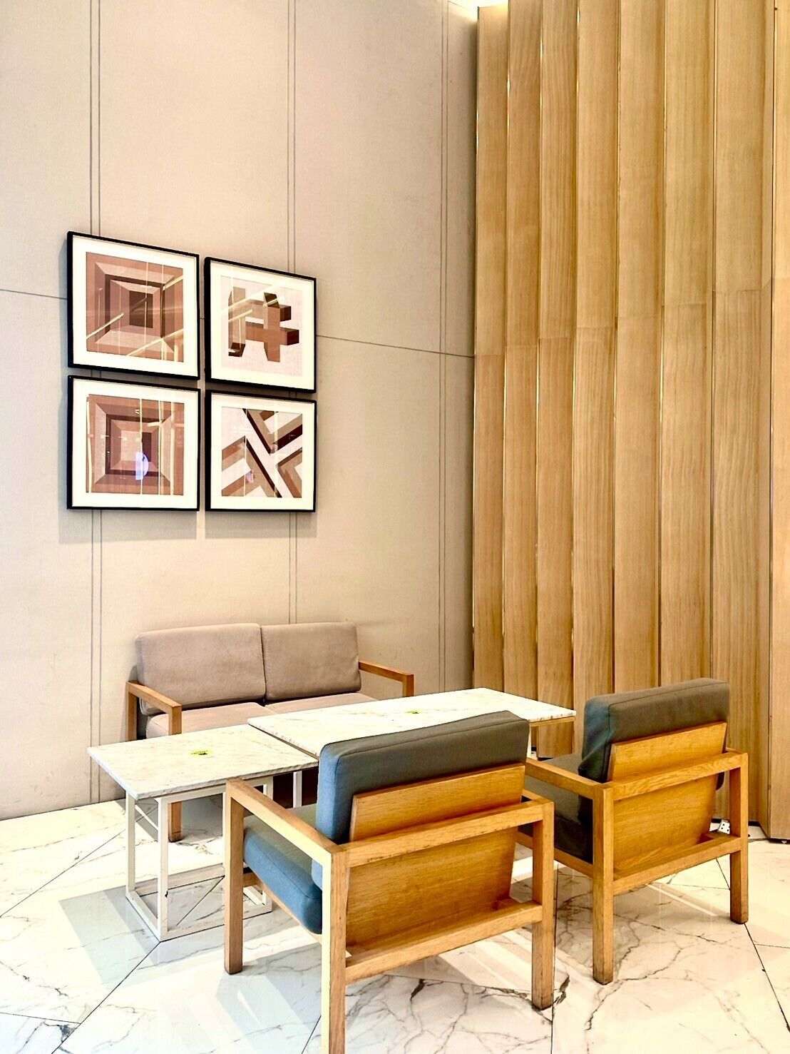 Una habitación moderna con una mesa de madera y dos sillas, un sofá color beige y cuatro obras de arte enmarcadas en la pared.