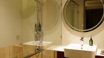 A modern bathroom with a glass-enclosed shower, a round mirror, and two sinks.