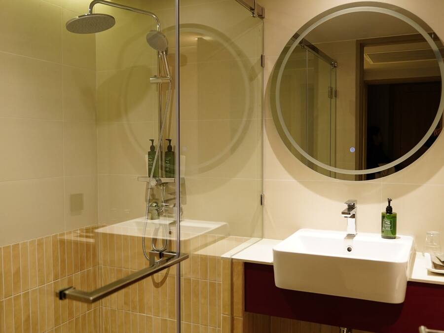 A modern bathroom with a glass-enclosed shower, a round mirror, and two sinks.