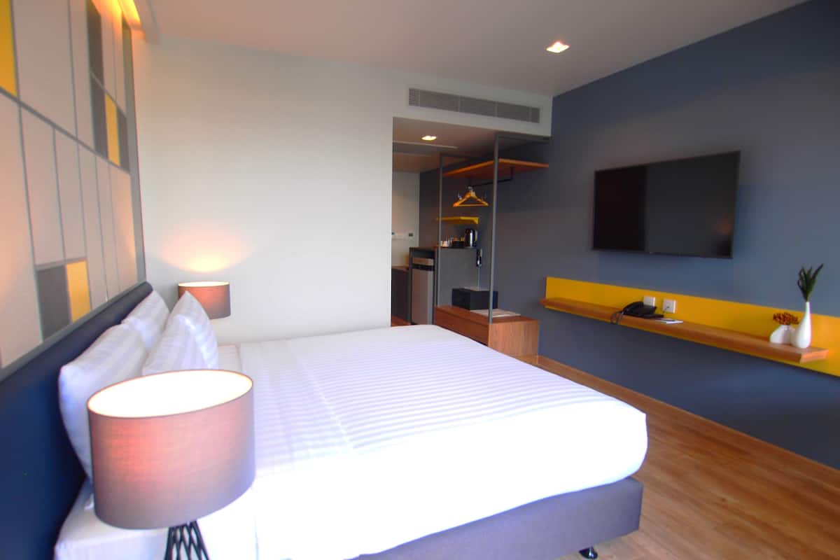 Een moderne hotelkamer met een groot bed, bedlampen, een aan de muur bevestigde televisie en een klein plankje met decoratieve objecten.