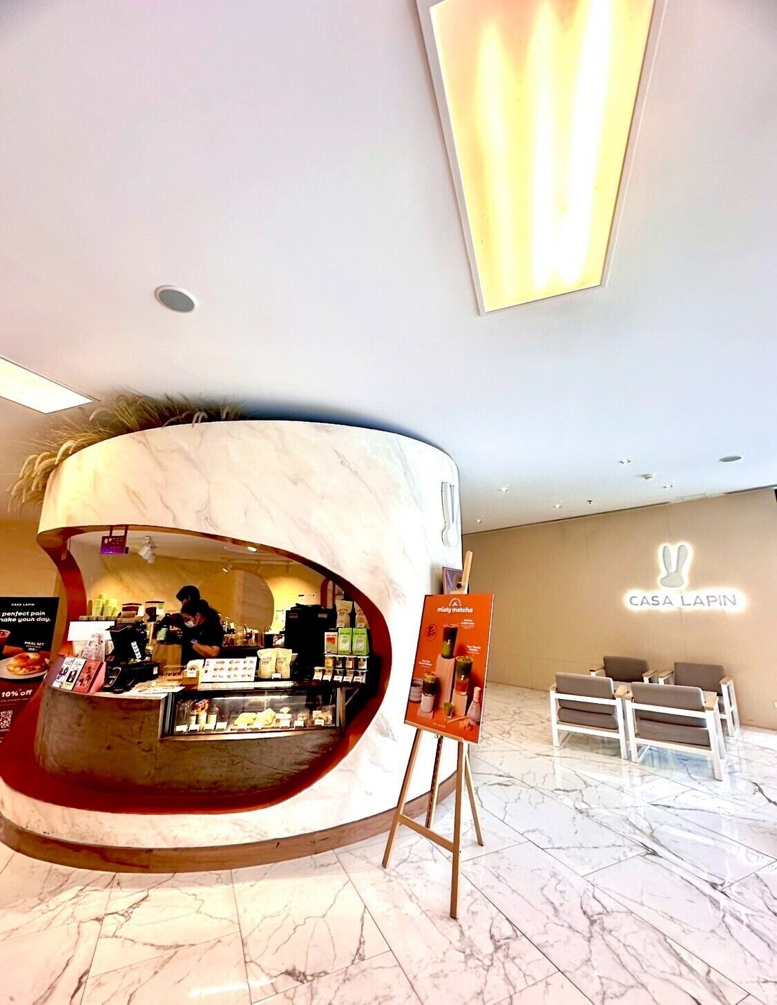A modern hotel lobby with a curved reception desk, a seating area, and a wall-mounted sign for 'Casa Lapin'.