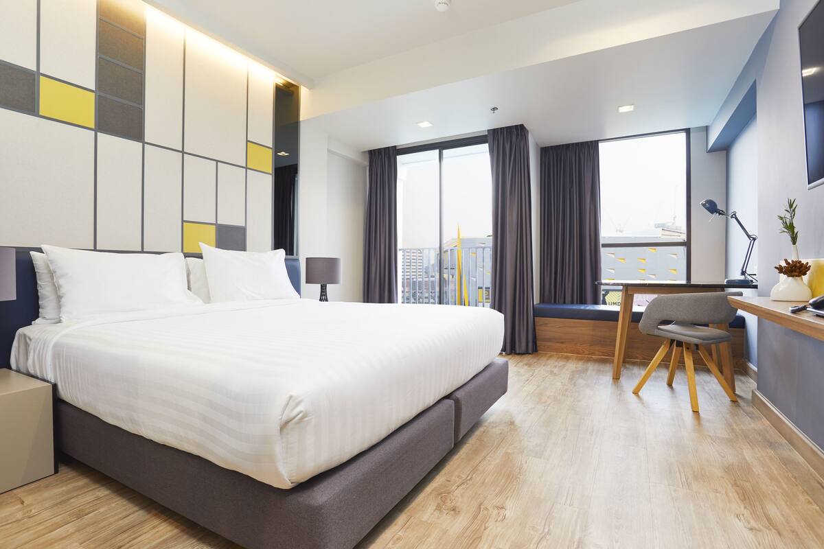 Een moderne hotelkamer met een groot bed, een bureau en uitzicht op de stad.