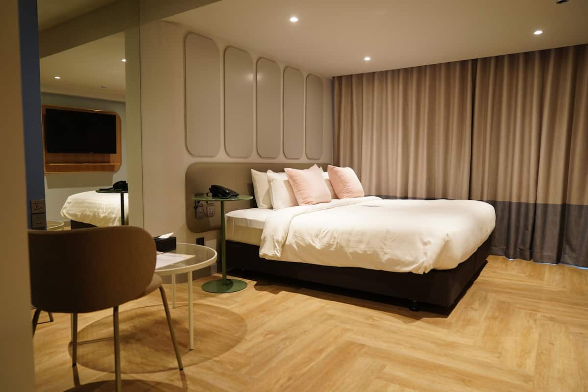 Een moderne hotelkamer met een groot bed, een klein rond tafeltje, een stoel, een nachtkastje met een lamp en een aan de muur bevestigde televisie.