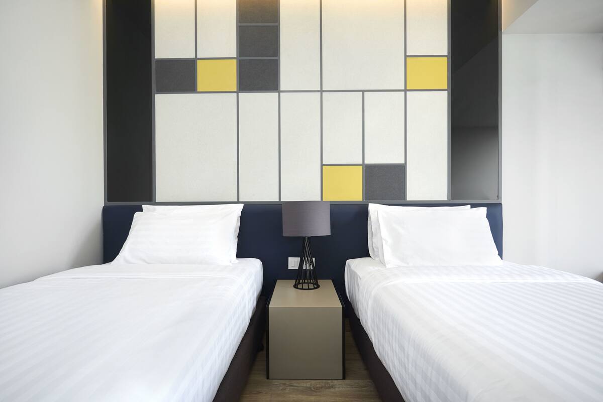 Een hotelkamer met twee enkele bedden, een nachtkastje met een lamp en een modern wandontwerp.