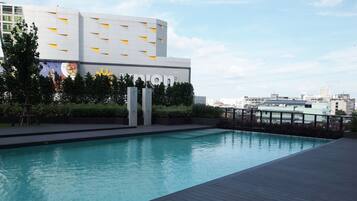 A modern building with a pool area, featuring a clear sky and urban skyline in the background.