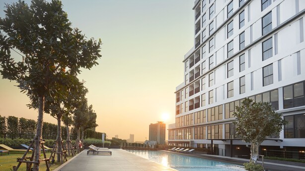 A modern hotel with a rooftop pool, surrounded by trees and a city skyline in the background.