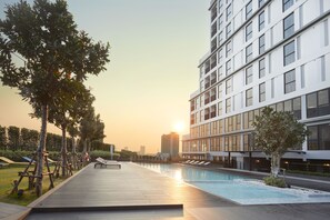 Un hotel moderno con piscina en la azotea, rodeado de árboles y un horizonte urbano al fondo.